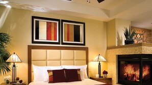 Habitación de hotel con una cama grande, dos obras de arte enmarcadas sobre la cama, una chimenea y una mesita de noche con lámpara.
