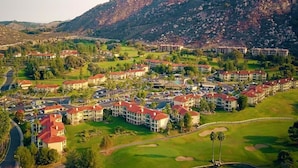 Un resort con varias construcciones, un campo de golf y terreno montañoso al fondo.