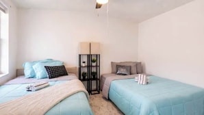 Une chambre avec deux lits, une table de chevet, une lampe et une étagère avec des plantes.