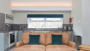 A modern kitchen with a window, a sofa with teal cushions, and a small table.