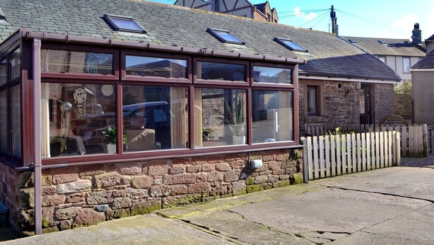 A stone house with a large bay window and a wooden fence. - The Milking Parlour - UK30866 (St Bees, near Whitehaven)