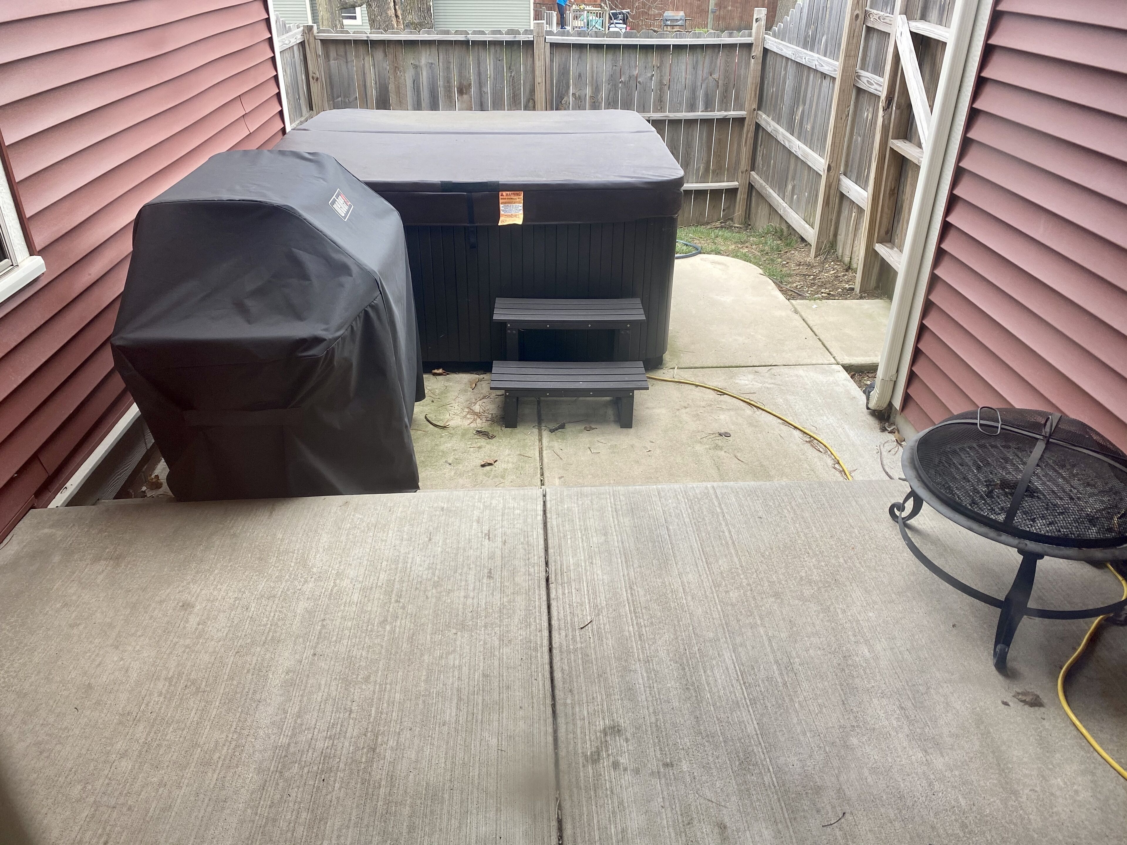 Una vasca idromassaggio coperta e un barbecue in un giardino con un patio in legno e un cortile in cemento.