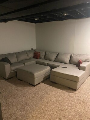 Um sofá modular com chaise, um banquinho e um controle remoto sobre o sofá.