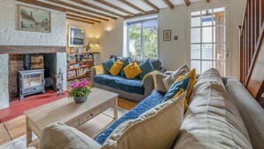 Una sala de estar acogedora con vigas de madera a la vista, una chimenea, un sofá con cojines, una mesa de centro y una estantería.