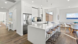 Una cocina moderna con muebles blancos, electrodomésticos de acero inoxidable y una isla central con taburetes de bar.