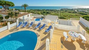 Un espace piscine aménagé sur le toit, avec des chaises longues bleues et une table, offrant une vue sur un paysage côtier.