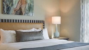 A hotel room with a bed, a ceiling fan, a nightstand with a lamp, and a painting on the wall.