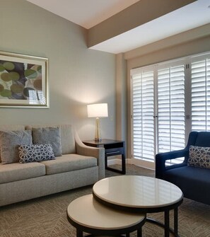 Relax in this inviting space with a comfortable sofa, small table, and lamp, surrounded by large windows and a beautiful piece of artwork.
