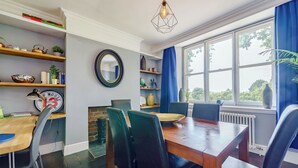 A dining area with a wooden table, black chairs, a brick wall, and a window with blue curtains. - A lovely three bedroom home, perfect for friends and family alike. (Bridstow, near Ross-on-Wye)