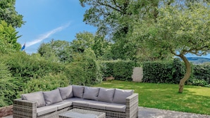 A wicker sectional sofa with grey cushions and a matching ottoman on a patio with stone flooring. - A lovely three bedroom home, perfect for friends and family alike. (Bridstow, near Ross-on-Wye)