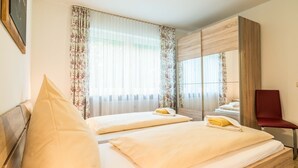 Een hotelkamer met twee bedden, een houten garderobe, een rode stoel en een grote spiegel.