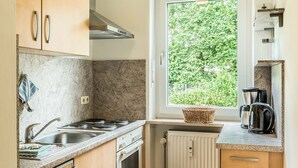 Een kleine keuken met een raam, een fornuis, een gootsteen en een koffiezetapparaat.