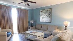 A living room with a sofa, a coffee table, a lamp, and a painting on the wall. - Havens 423 with Pool View! Great Location! (North Myrtle Beach)
