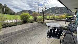 Patio esterno con tavolo e sedie, circondato da un vialetto in ghiaia e vegetazione, con vista su un paesaggio collinare.