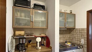 Una cucina compatta con mobili in legno, un forno a microonde, una moka e un lavello.