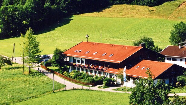 Un hotel rurale con tetto in tegole rosse, immerso in campi verdi e colline boschive.