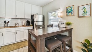 A modern kitchen with white cabinets, a stainless steel refrigerator, and a wooden dining table with four chairs. There are two framed seahorse paintings on the wall. - Dunedin Cottage on Pinellas Trail w/ Heated Pool, Walk or Bike to Downtown Dunedin! (Dunedin)