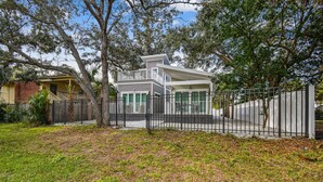 A modern two-story house with a balcony, surrounded by a black metal fence and trees. - Dunedin Cottage on Pinellas Trail w/ Heated Pool, Walk or Bike to Downtown Dunedin! (Dunedin)