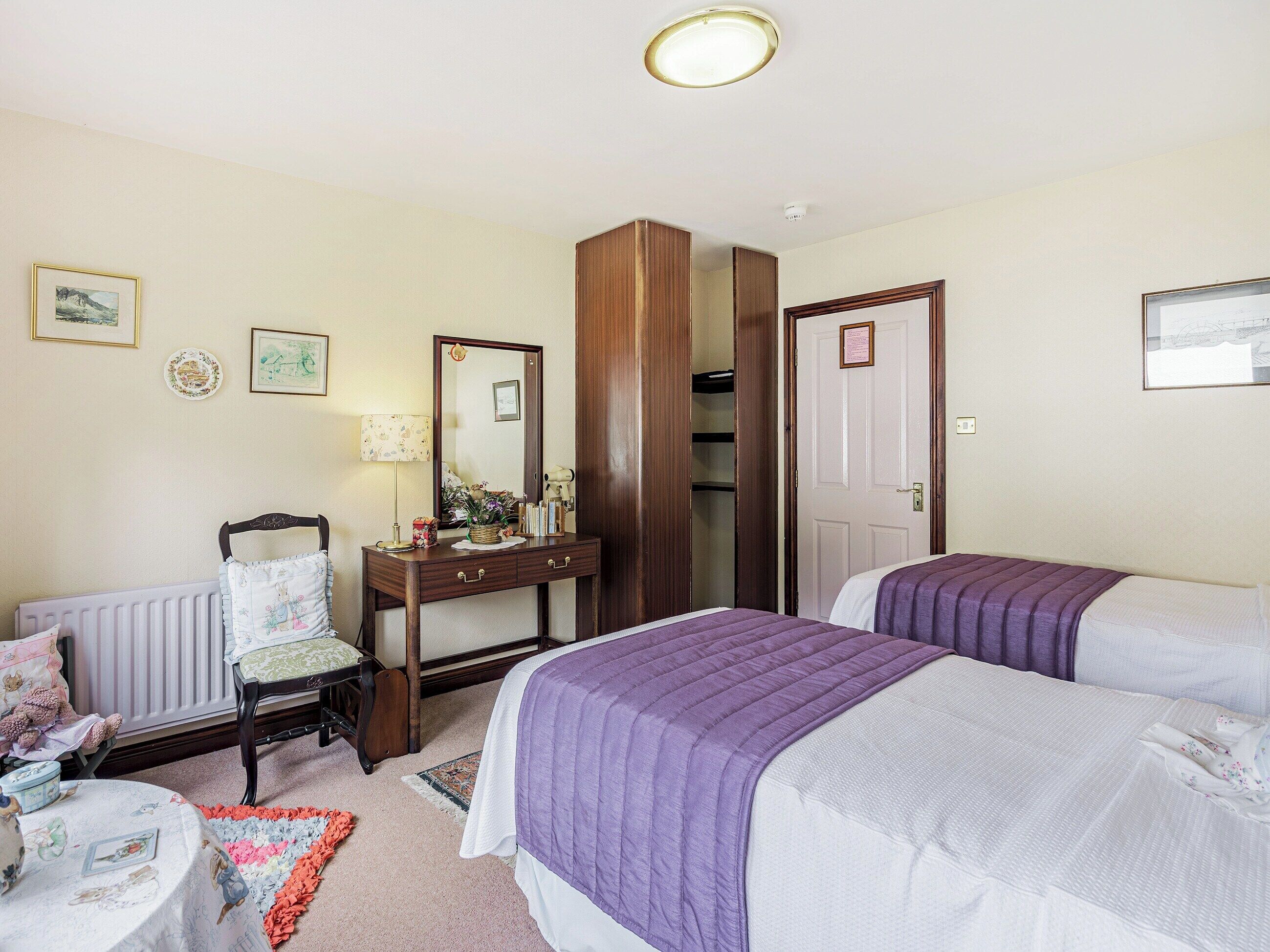 A bedroom with two beds, a dresser, a chair, a radiator, and a mirror.