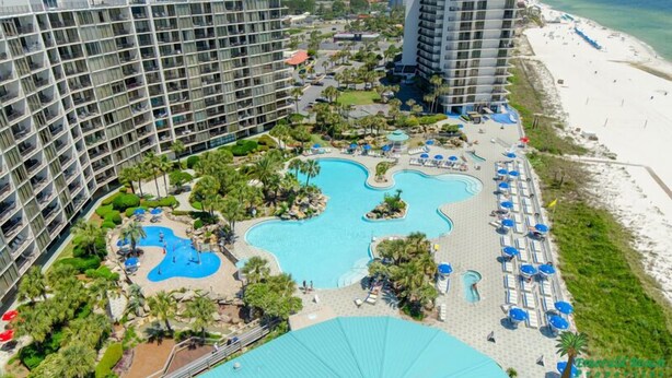 A hotel with multiple high-rise buildings, a large swimming pool area with various water features, and a beach adjacent to the property.