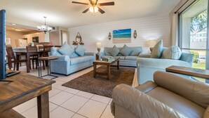 A spacious living room with a large sofa set, a coffee table, and a dining area with chairs and a table.