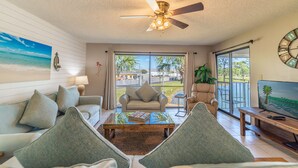 A spacious living room with a ceiling fan, a large window, and a view of the outdoors.