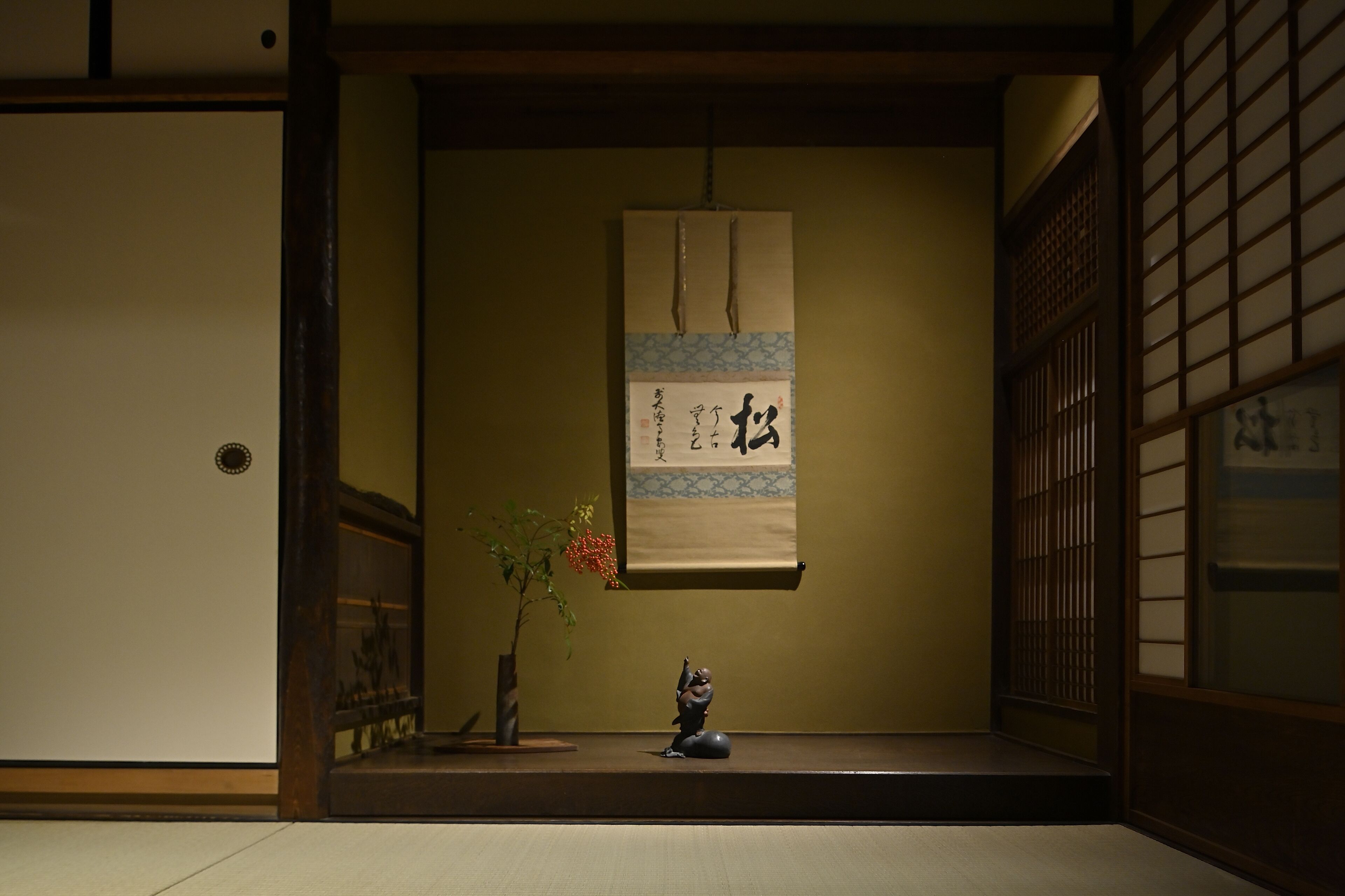 A traditional Japanese room with tatami flooring, a shoji screen, and a hanging scroll with calligraphy.