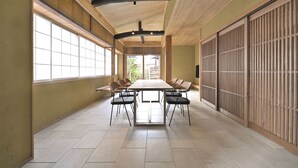 Une pièce spacieuse avec une longue table et des chaises, de grandes fenêtres et une porte coulissante traditionnelle.