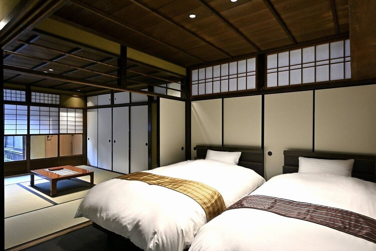 Une pièce de style japonais traditionnel, avec un sol recouvert de tatamis, deux lits avec du linge de lit blanc, un plafond en bois et des portes coulissantes de type shoji.