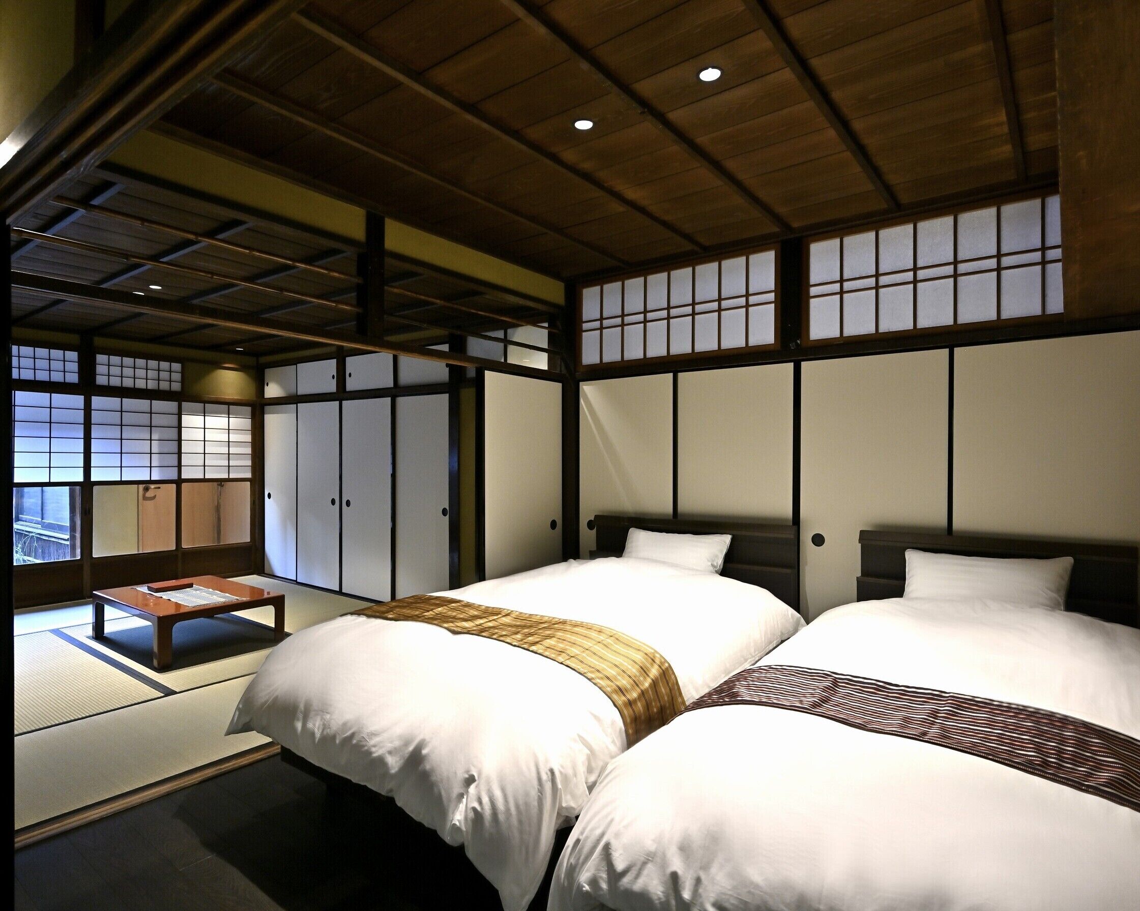 Ein traditionelles japanisches Schlafzimmer mit Tatami-Böden, zwei Betten mit weißer Bettwäsche und verschiebbaren Shoji-Türen.