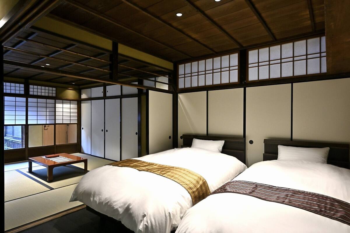 Une chambre de style japonais traditionnel, avec un sol recouvert de tatamis, deux lits avec une literie blanche et des portes coulissantes de type shoji.
