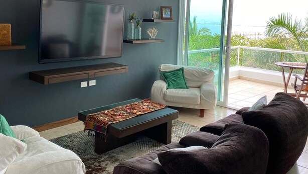 Una sala de estar moderna con una televisión de pantalla plana, un sofá, una mesa de centro y un balcón con vistas.