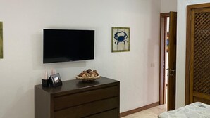 Una habitación con una televisión de pantalla plana montada en la pared, un aparador de madera con cajones, una cesta pequeña con adornos y un cuadro enmarcado.