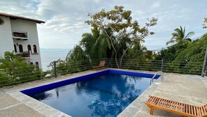 Una piscina rectangular con revestimiento azul, rodeada por una terraza de piedra.