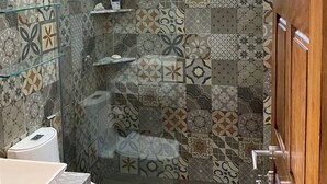 Un baño con baldosas estampadas, cabina de ducha de vidrio, inodoro y lavabo con encimera de mármol.