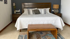 Un dormitorio con una cama grande, cabecera de madera, mesita de noche con lámpara y un banco.