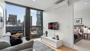 Ett modernt vardagsrum med ett stort fönster, en platt-TV, en soffa, ett soffbord och en säng.