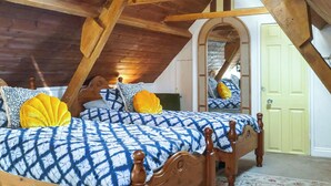 A bedroom with a sloped ceiling, wooden beams, a bed with patterned bedding, and a mirror reflecting the room. - 3 bedroom accommodation in Polperro, near Looe (Polperro, near Looe)