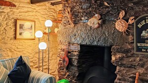 A cozy room with a stone fireplace, a striped sofa, and a framed picture on the wall. - 3 bedroom accommodation in Polperro, near Looe (Polperro, near Looe)