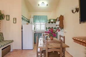 Cucina compatta con zona pranzo, frigorifero, lavello e finestra con tenda a quadri.