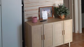 Een keuken met een flatscreen televisie aan een houten wand, een witte koelkast, een houten kastje met een fotolijstje en een roze mok, en een potplant op het aanrecht.