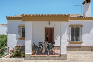 A white building with a tiled roof, a door, and a small patio with a table and chairs.