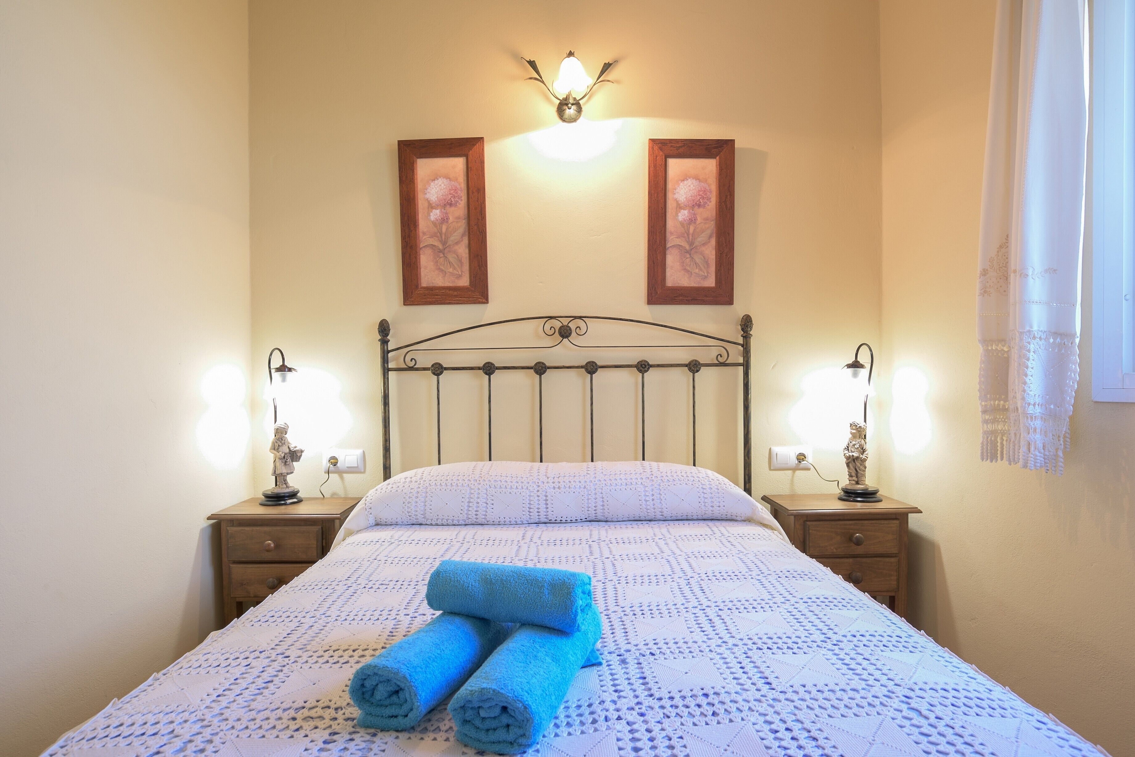 Un lit bien fait, agrémenté de serviettes bleues roulées, de deux cadres-photos accrochés au mur et de lampes de chevet posées sur des tables de nuit en bois.