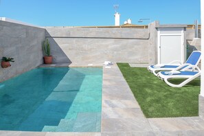 A rooftop pool with clear blue water, a small grassy area, and two lounge chairs.