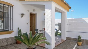 A house with a white exterior, a wooden door, a small patio with a table and chairs, and a potted plant. - Beautiful Accommodation "Casa Clavel" with Private Pool, Air Conditioning and Terrace (Conil de la Frontera)