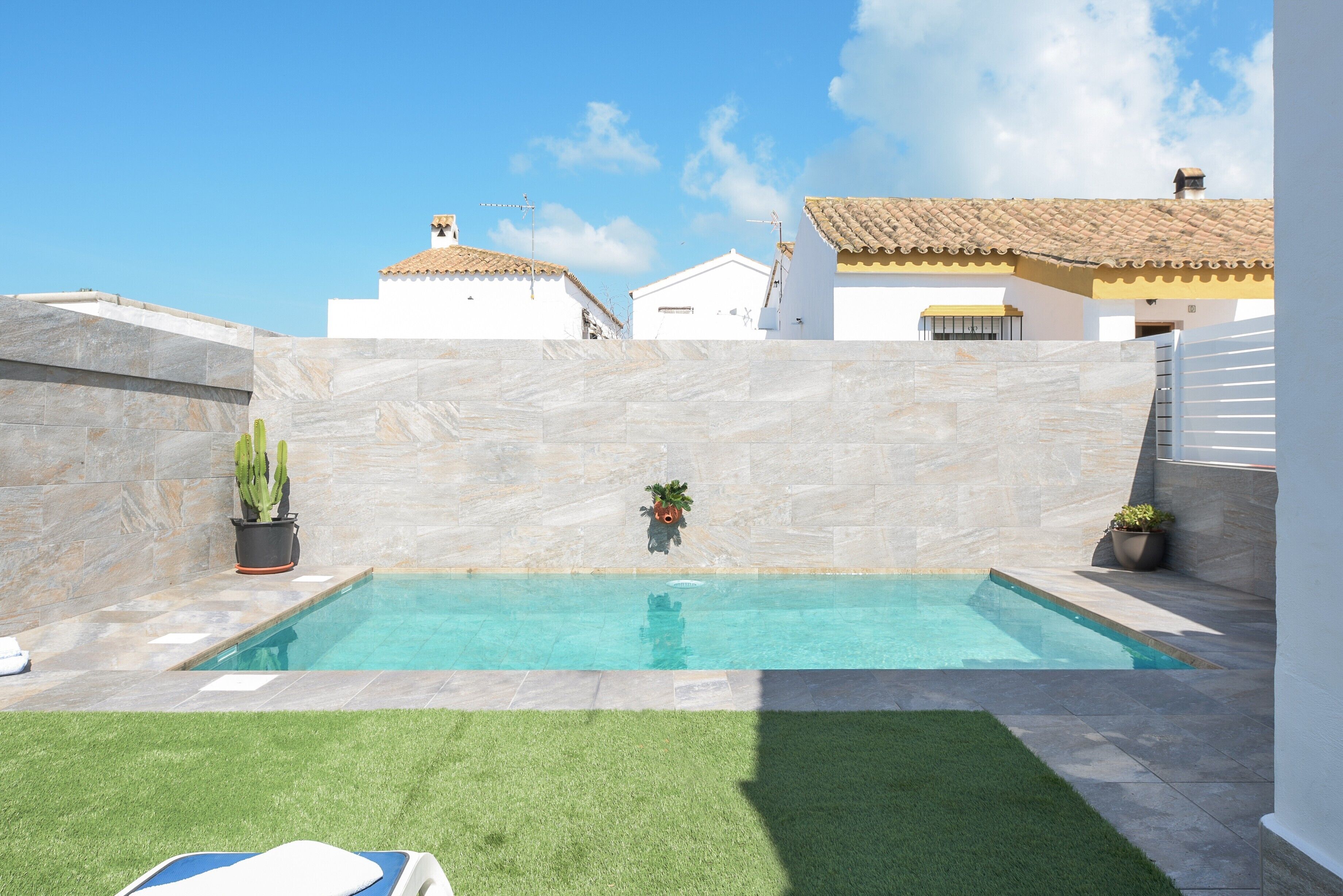 A swimming pool with a tiled deck, surrounded by a low wall and potted plants.