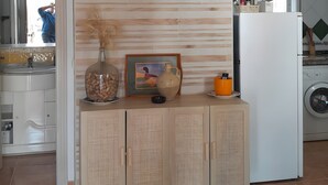 A modern kitchen with a flat-screen TV mounted on a wooden panel wall, a white cabinet with decorative items, and a washing machine in the background. - Beautiful Accommodation "Casa Clavel" with Private Pool, Air Conditioning and Terrace (Conil de la Frontera)