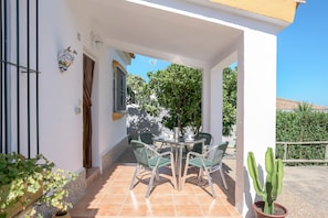 A covered patio with a table and chairs, a potted cactus, and a window with a curtain. - Beautiful Accommodation "Casa Clavel" with Private Pool, Air Conditioning and Terrace (Conil de la Frontera)