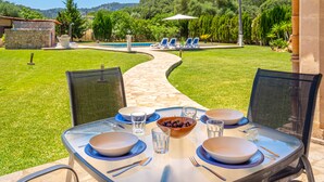 An outdoor dining area with a table set for two, a bowl of fruit, and a pool in the background. - Rural Country House with Pool, Wi-Fi, Lawn and Veranda (POLLENSA)