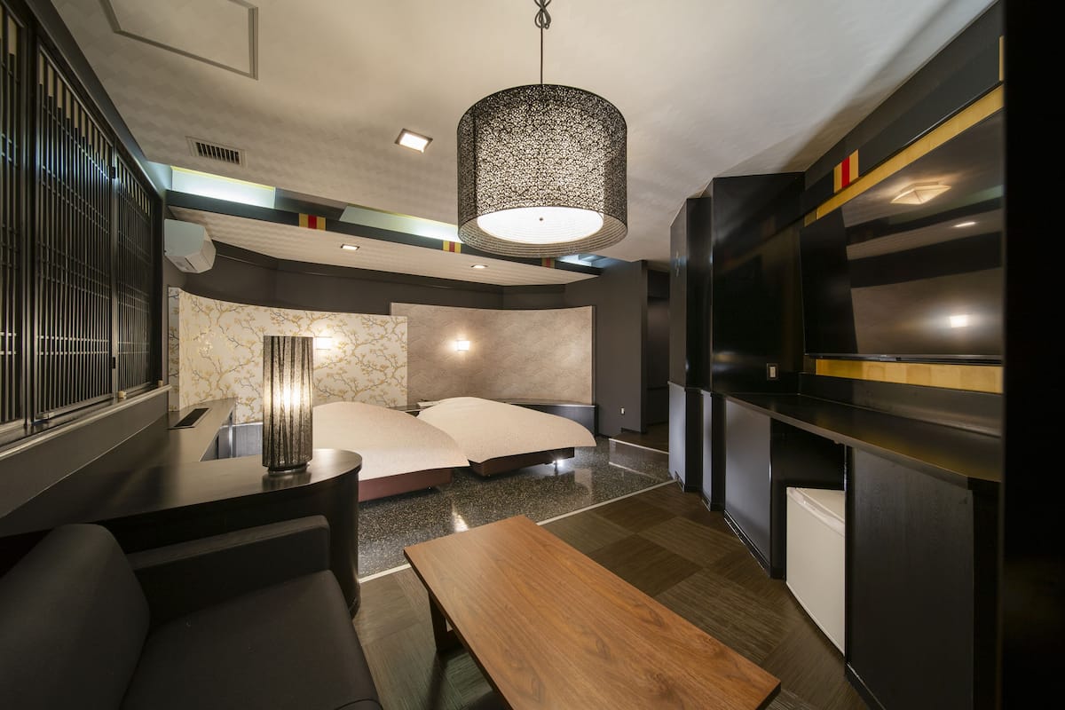 Een moderne hotelkamer met een bed, een houten bankje, een tafel, een televisie en een bijzondere lamp met een uniek patroon.